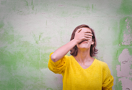 Woman standing against wall with hand to her forehead