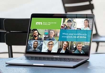 Laptop on a table in a cafe. The laptop shows a PowerPoint presentation for Minnesota Dual-Training Pipeline. A series of images of employees across sectors with the headline: When your workforce is energized, we all thrive.