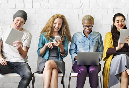 line of people sitting on a bench each one holding a digital tablet or laptop