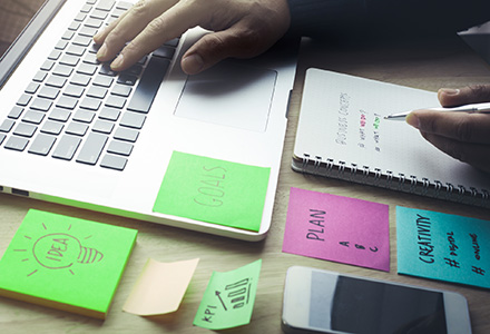 Business person working on laptop, notebook, and with Post-its to develop strategy