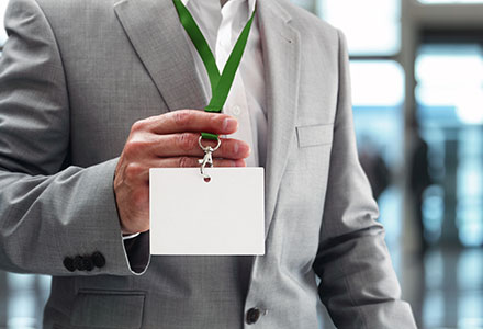 Man in a suit holding up a blank nametag on a lanyard.