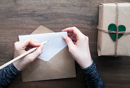 Hands writing a personal note and placing it in a crafted envelope