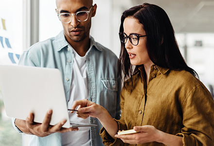 Man and woman coworkers comparing mobile phone and laptop content in an office