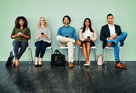 Row of diverse people sitting in chairs with electronic devices