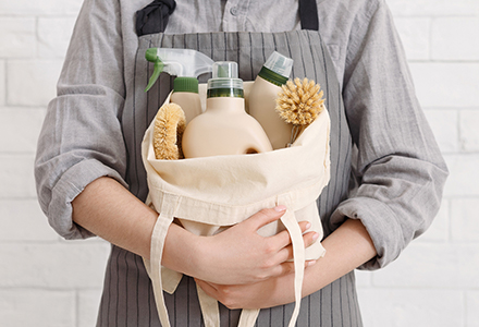 Person in an apron holding a bag of cleaning supplies