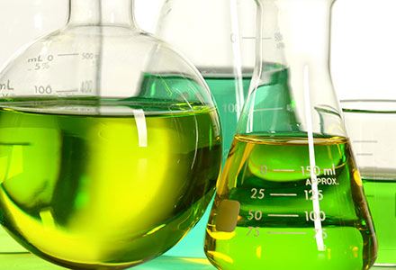 A photo of a series of beakers in a laboratory filled with a green solution